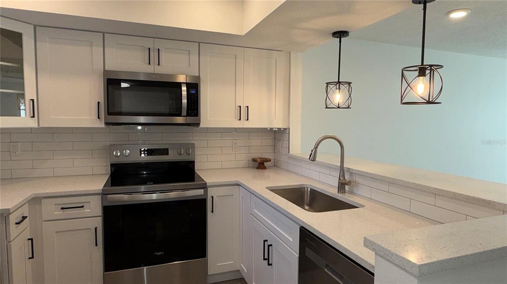 A kitchen features white cabinets, stainless steel appliances, quartz countertops, and a subway tile backsplash — 4805 ALT 19 UNIT 311, PALM HARBOR, FL