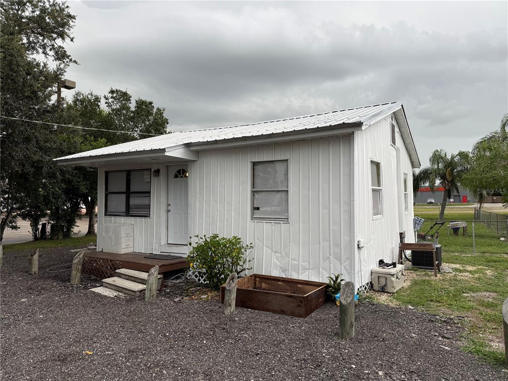 A small, white, metal-sided house with a front porch and a gravel yard — 101 S ROGERS AVENUE, ARCADIA, FL