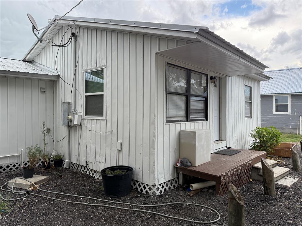 The exterior of a white, vertical-sided house features a small wooden porch and metal roof — 101 S ROGERS AVENUE, ARCADIA, FL