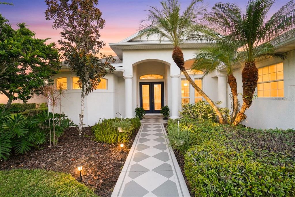A white house exterior features a diamond-patterned walkway leading to a dark double front door — 16203 33RD COURT E, PARRISH, FL