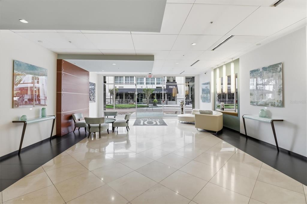 A modern building lobby features a polished tile floor, seating areas, and glass entrance doors — 101 S EOLA DRIVE UNIT 1104, ORLANDO, FL
