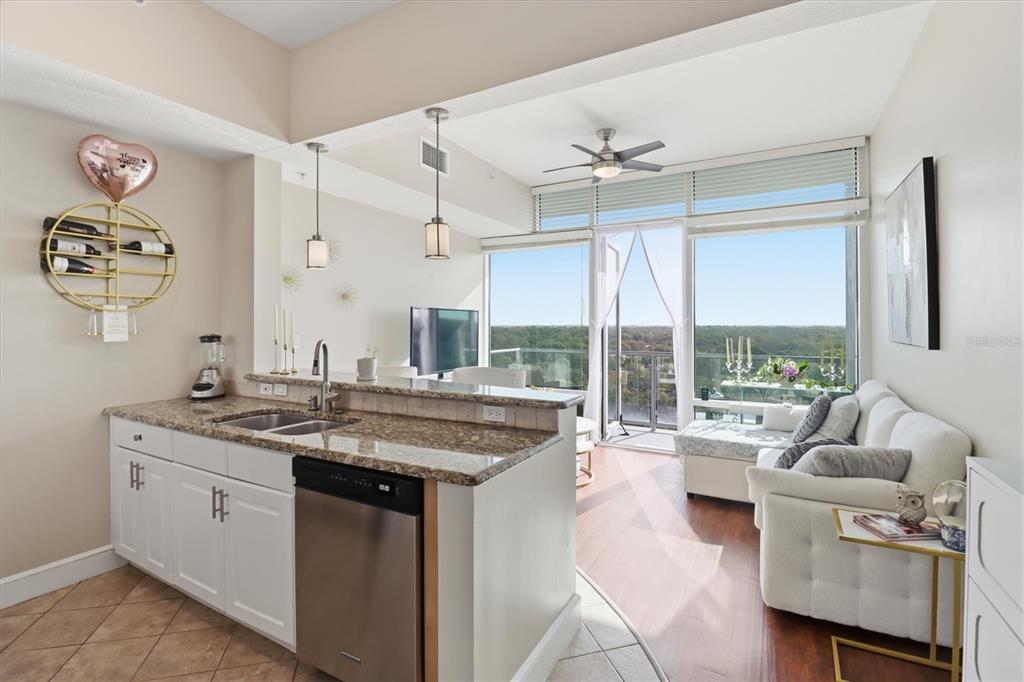 A kitchen with granite countertops and white cabinets opens into a living area with balcony views — 101 S EOLA DRIVE UNIT 1104, ORLANDO, FL