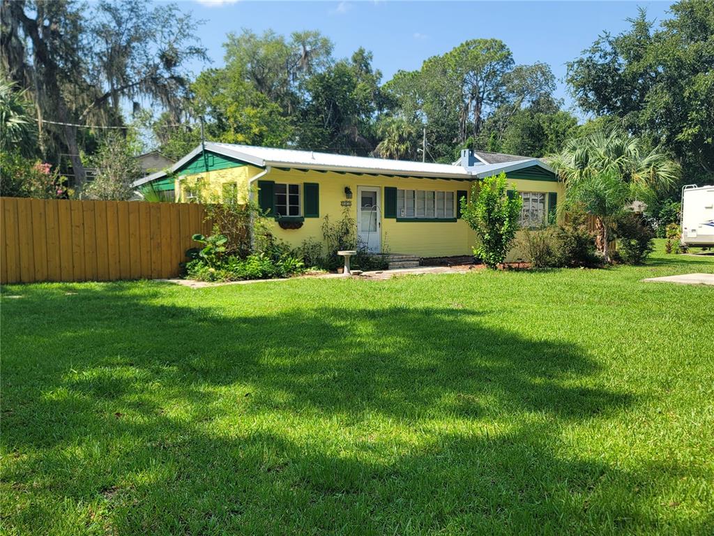 A yellow single-story house with green shutters and a metal roof sits on a lawn — 962 NE 5TH STREET, OCALA, FL