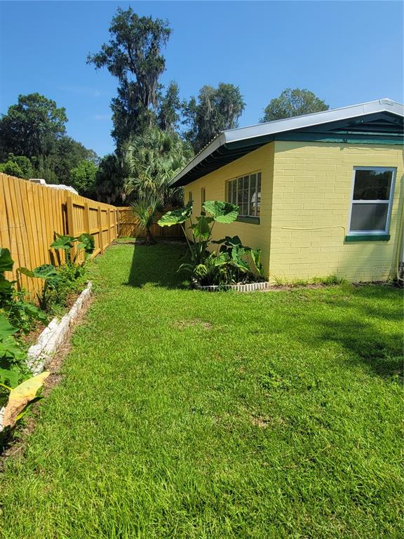 A yellow concrete block house sits next to a wooden fence and a grassy yard — 962 NE 5TH STREET, OCALA, FL