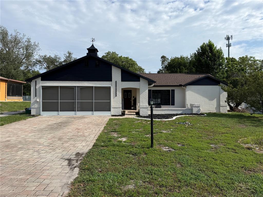 A single-story house with a white brick facade, dark blue siding, and a paved driveway — 8185 PHILATELIC DRIVE, SPRING HILL, FL
