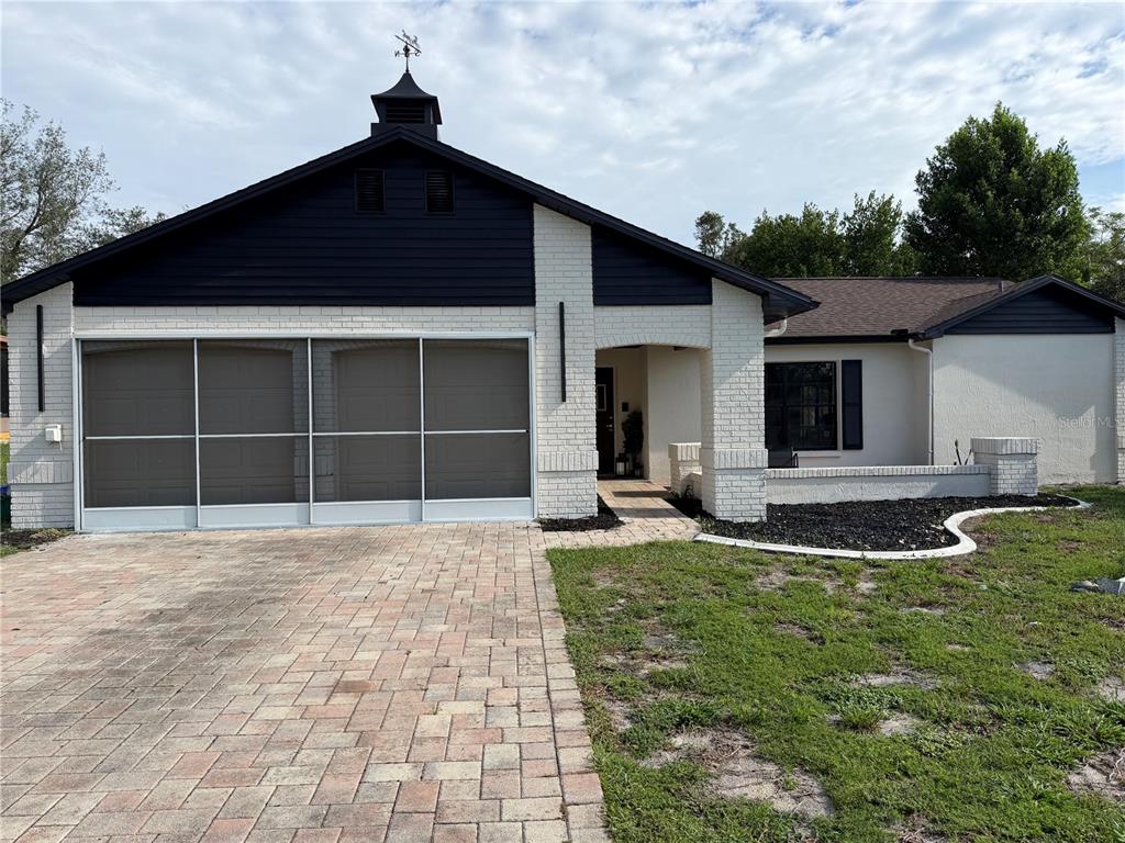 A single-story house with a white brick facade, dark siding, and a screened garage door — 8185 PHILATELIC DRIVE, SPRING HILL, FL