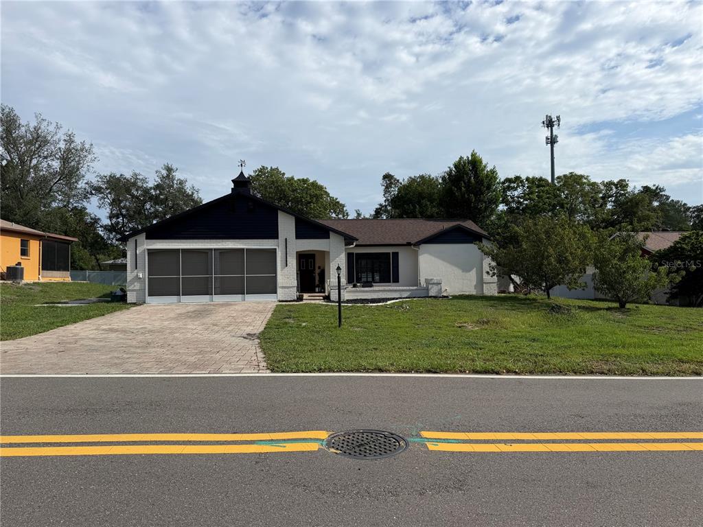A single-story house with a white brick facade, dark blue accents, and a screened garage — 8185 PHILATELIC DRIVE, SPRING HILL, FL