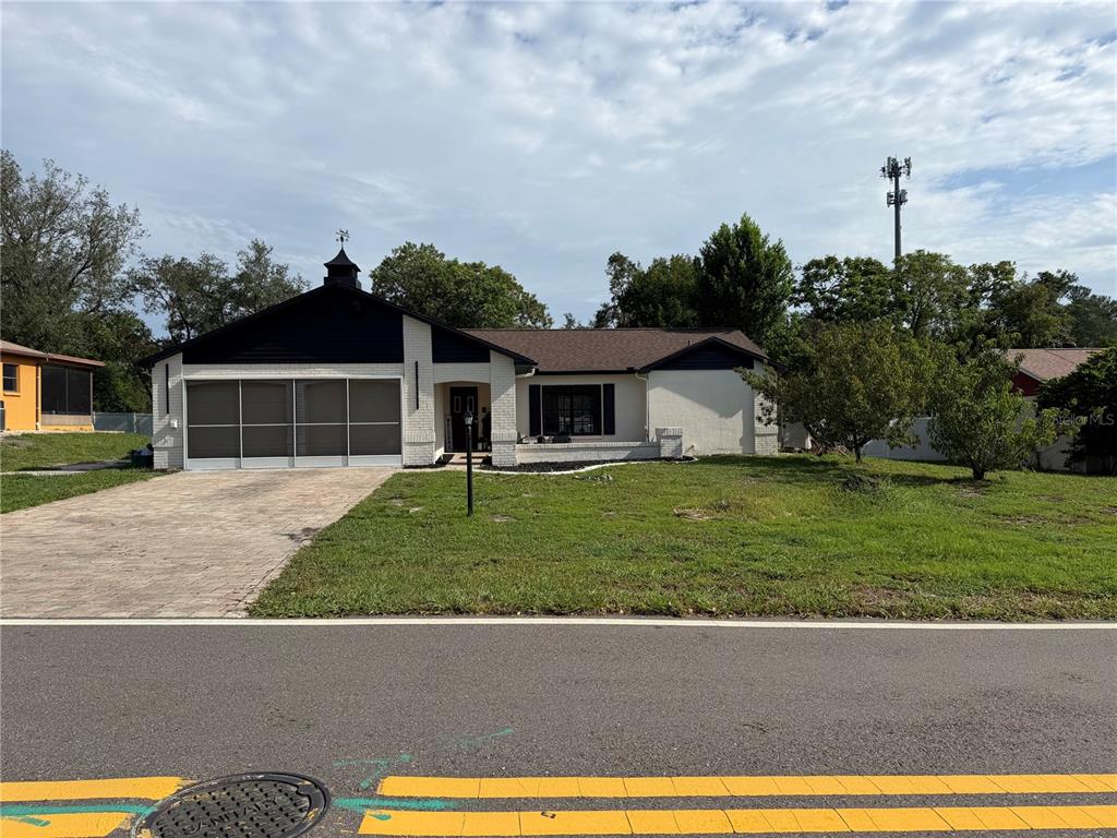 A single-story house features a brick facade, a dark gable roof, and a paved driveway — 8185 PHILATELIC DRIVE, SPRING HILL, FL
