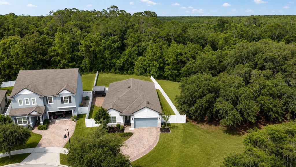 An aerial view shows two suburban houses with paved driveways and white fences bordering woods — 3485 MIDDLEBROOK PLACE, HARMONY, FL