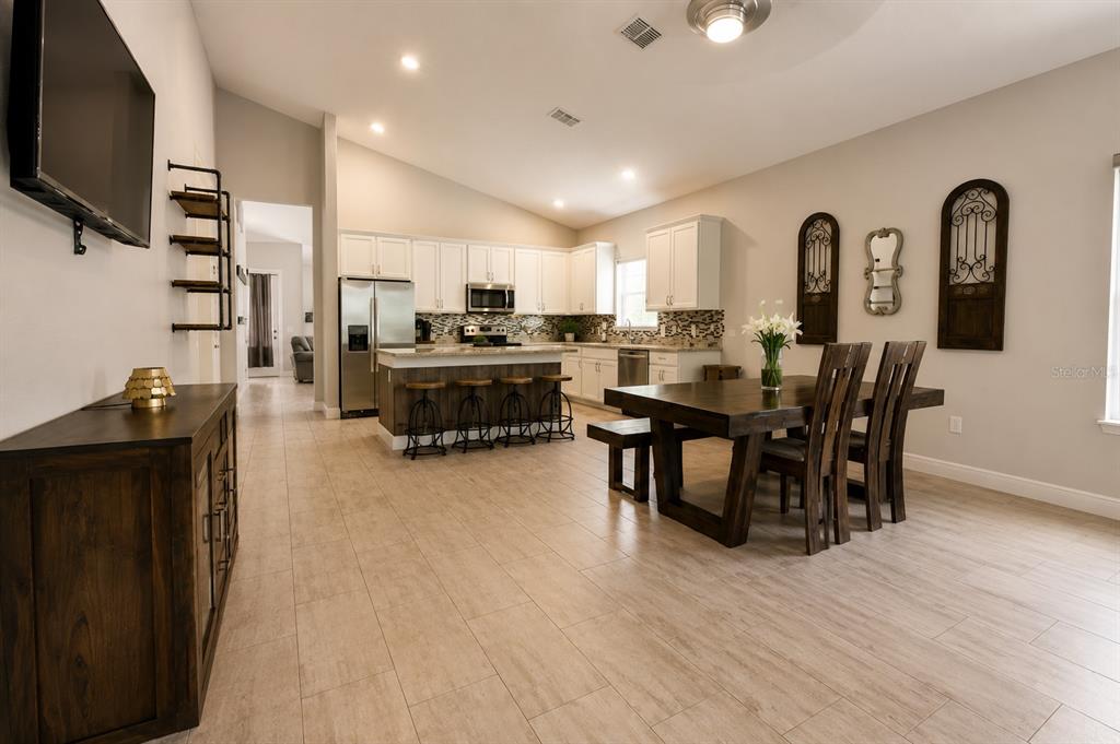 An open-concept kitchen and dining area features white cabinets, a wood island, and tile flooring — 3485 MIDDLEBROOK PLACE, HARMONY, FL