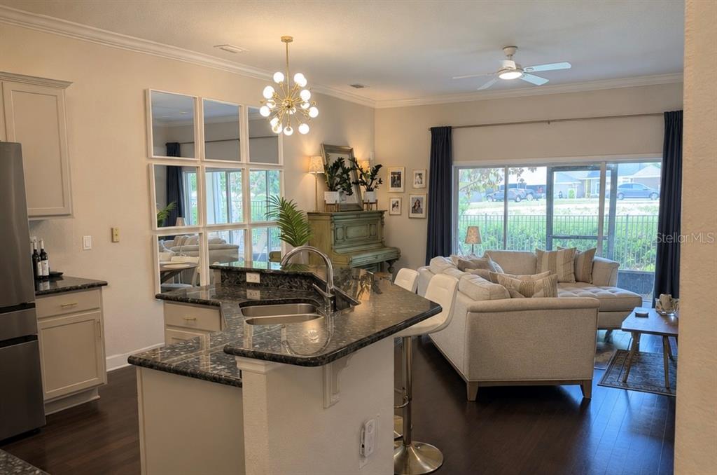 An open-concept kitchen with granite countertops overlooks a living room with a sliding glass door — 1018 GREEN GATE BOULEVARD, GROVELAND, FL