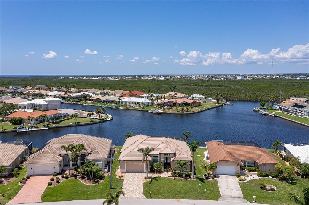 An aerial view shows three suburban houses situated along a canal with a distant horizon — 3967 SAN PIETRO COURT, PUNTA GORDA, FL