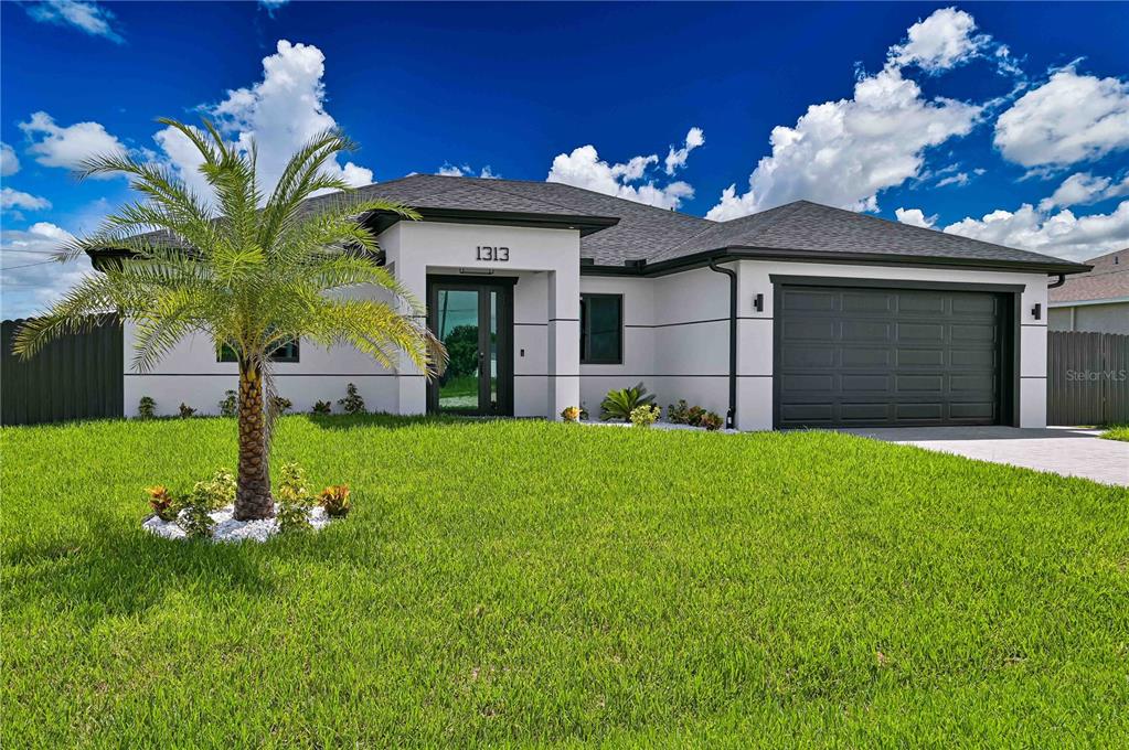A modern single-story house with a white exterior, dark trim, and a palm tree in front — 1313 NE 7TH AVENUE, CAPE CORAL, FL