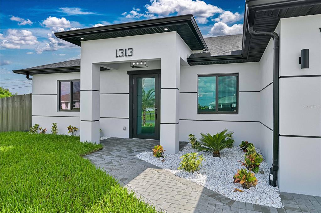 The exterior of a modern white house features a paved walkway and a glass front door — 1313 NE 7TH AVENUE, CAPE CORAL, FL