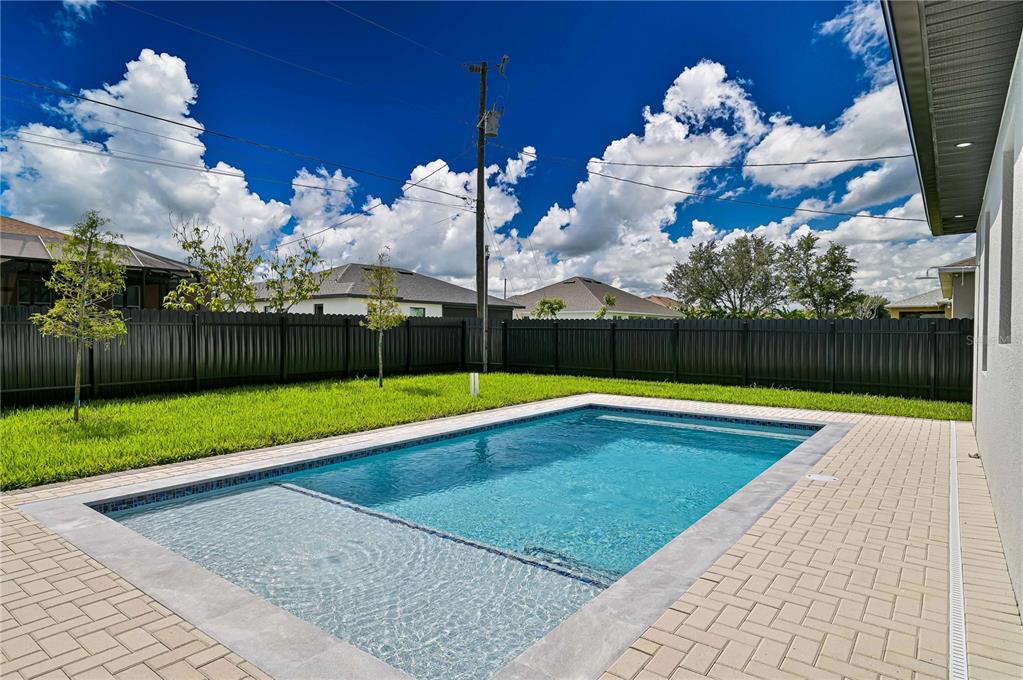 A rectangular swimming pool with a tanning ledge sits in a fenced backyard with pavers — 1313 NE 7TH AVENUE, CAPE CORAL, FL