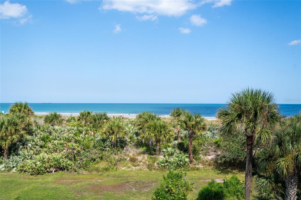 A view of a sandy beach and ocean framed by lush green palm trees — 8700 RIDGEWOOD AVENUE UNIT 205B, CAPE CANAVERAL, FL