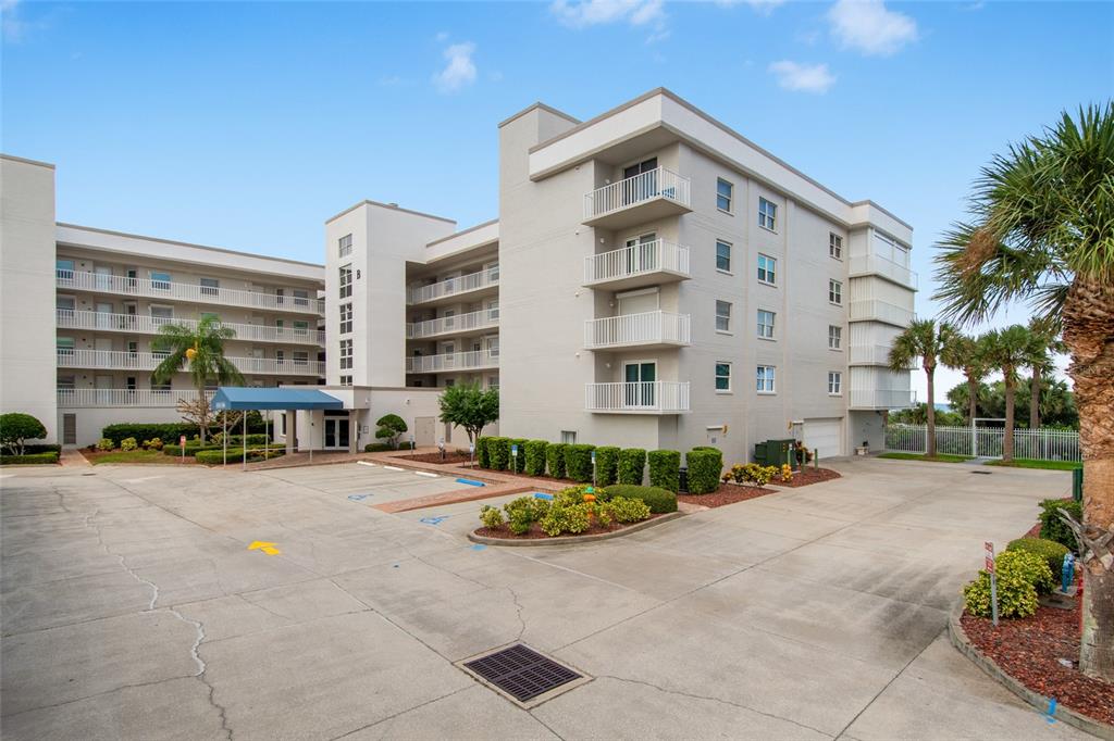 A multi-story apartment building with balconies and a parking lot in the foreground — 8700 RIDGEWOOD AVENUE UNIT 205B, CAPE CANAVERAL, FL