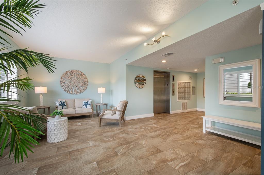 A bright lobby features light blue walls, tile flooring, a seating area, and an elevator — 8700 RIDGEWOOD AVENUE UNIT 205B, CAPE CANAVERAL, FL