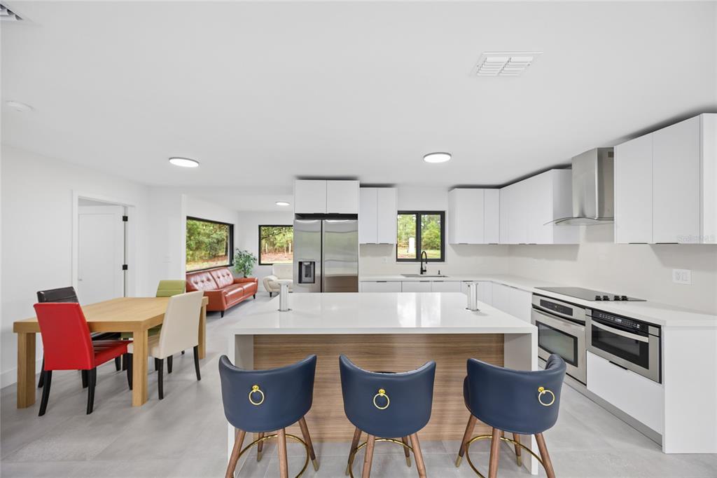 A modern kitchen features a large white island, blue bar stools, and stainless steel appliances — 241 SW BUENA VISTA ROAD, DUNNELLON, FL