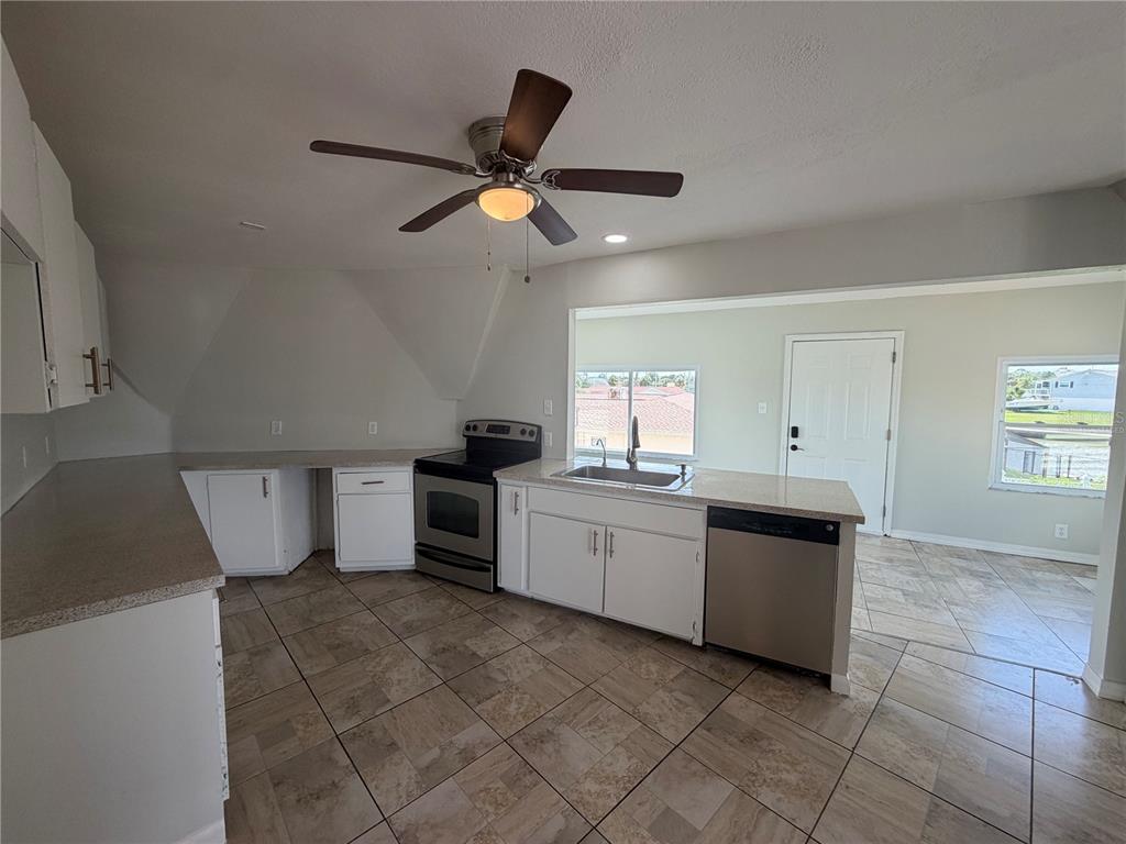 A kitchen with white cabinets, stainless steel appliances, and tile flooring opens to an adjacent room — 4100 FLAMINGO BOULEVARD, HERNANDO BEACH, FL
