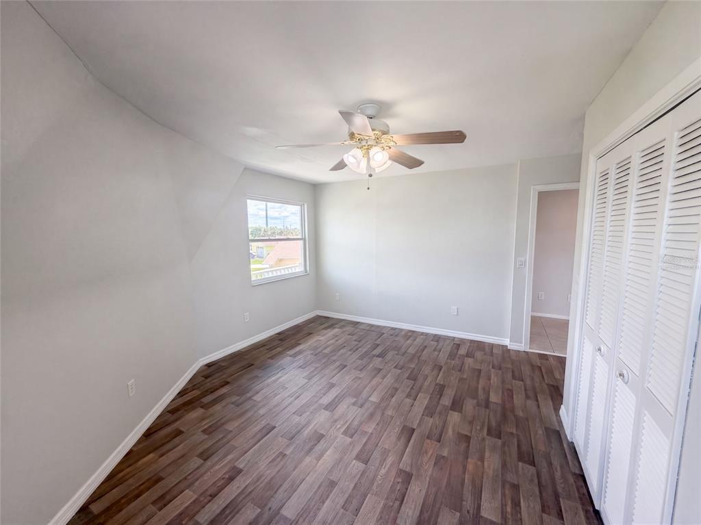 An empty bedroom with light gray walls, wood-look flooring, a ceiling fan, and louvered closet doors — 4100 FLAMINGO BOULEVARD, HERNANDO BEACH, FL