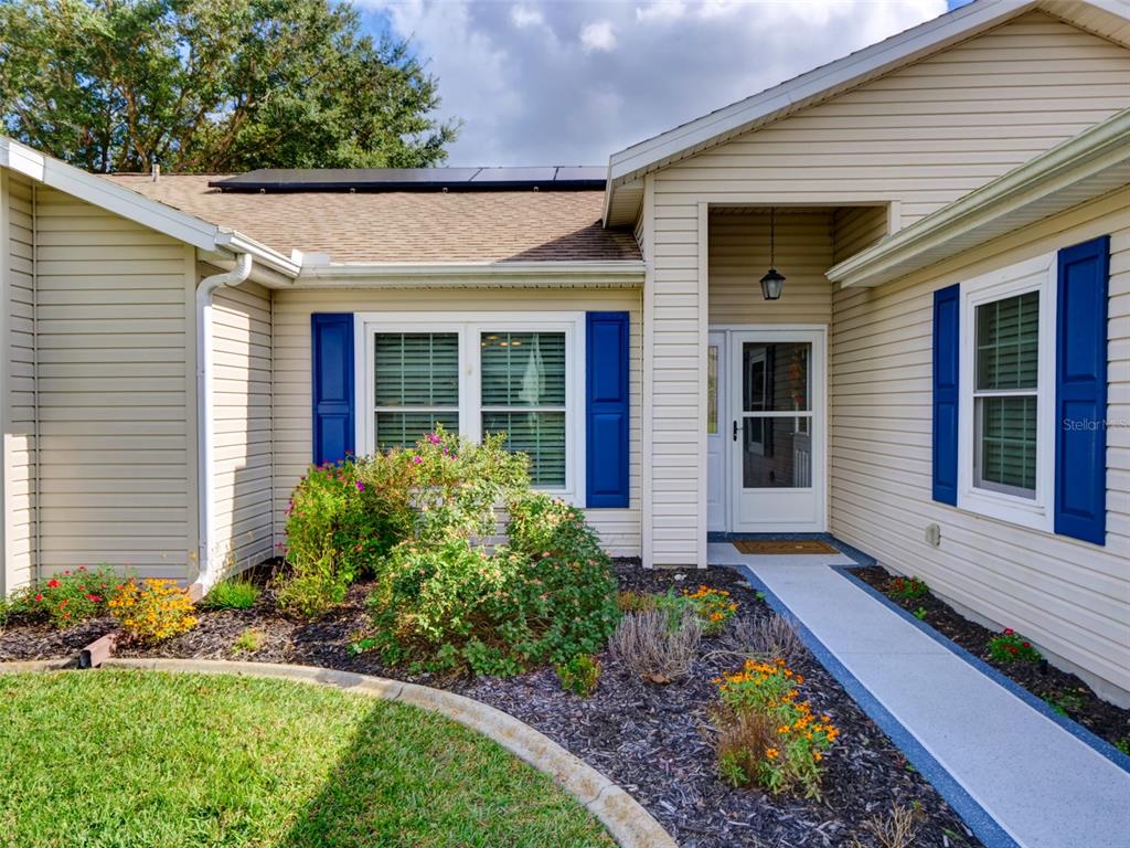 A tan house exterior features blue shutters, a front walkway, and a landscaped garden bed — 4704 RIVER RIDGE DRIVE, LEESBURG, FL