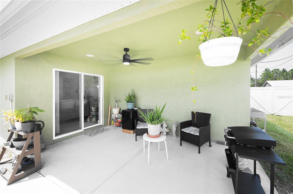 A covered concrete patio features a ceiling fan, sliding glass doors, and outdoor furniture — 615 FOURTH, BUNNELL, FL
