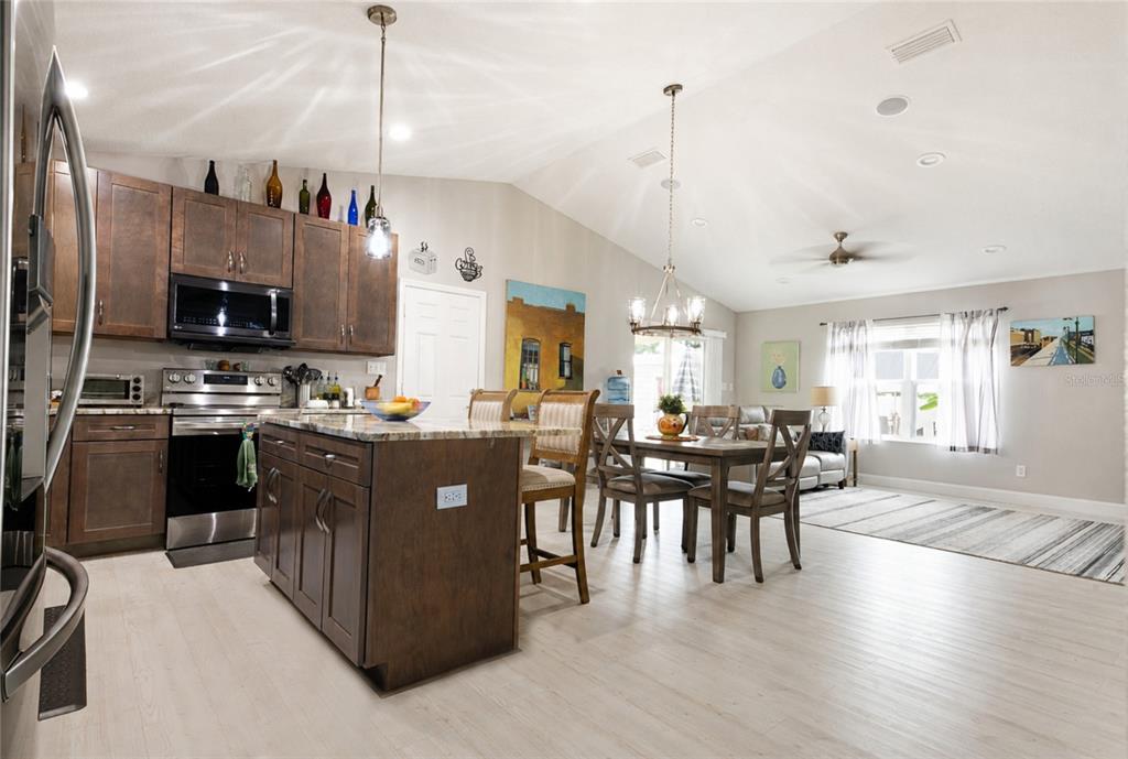 A kitchen with dark wood cabinets and a granite island flows into a dining area — 615 FOURTH, BUNNELL, FL