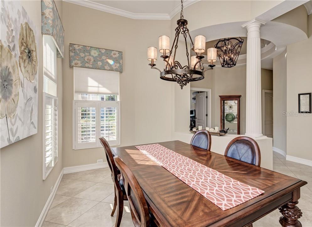 A dining room features a wooden table, a decorative chandelier, and white plantation shutters — 304 8TH AVENUE E, PALMETTO, FL