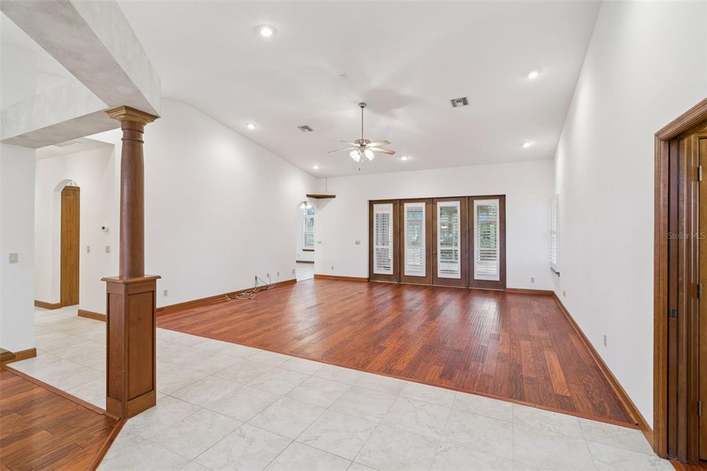 A spacious living room features hardwood flooring, white walls, a ceiling fan, and glass doors — 8516 FIRESTONE CIRCLE, CLERMONT, FL