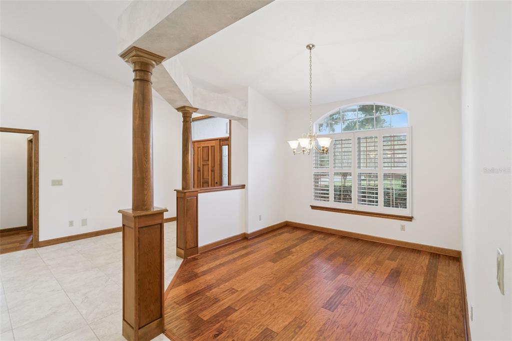 A dining room features hardwood floors, a chandelier, and wooden columns separating it from tile — 8516 FIRESTONE CIRCLE, CLERMONT, FL