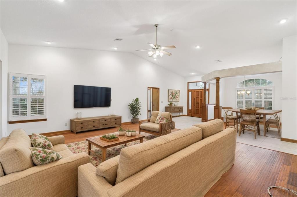A living room with a vaulted ceiling, hardwood floors, a television, and a dining area — 8516 FIRESTONE CIRCLE, CLERMONT, FL