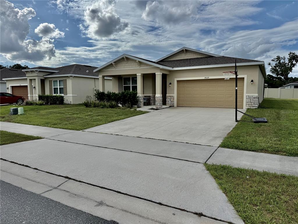 A single-story suburban house with a tan stucco exterior, stone accents, and a concrete driveway — 4029 MAYHILL LOOP, EUSTIS, FL