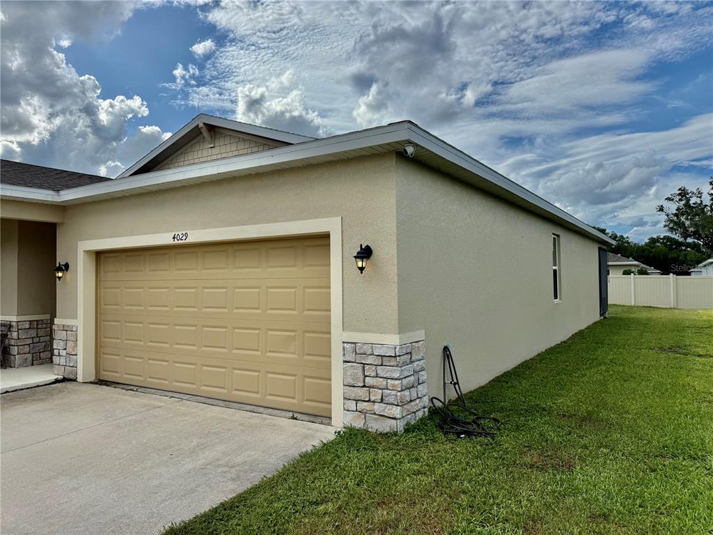 A beige house exterior features a two-car garage, stone accents, and a side lawn — 4029 MAYHILL LOOP, EUSTIS, FL