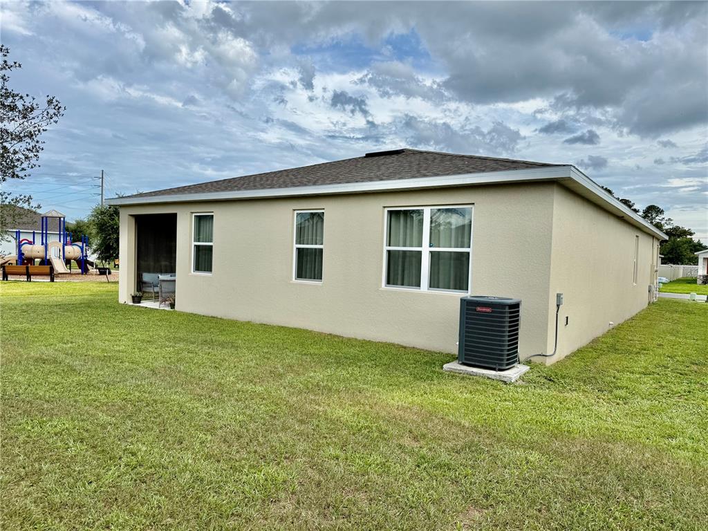 The exterior of a beige house features a small patio, several windows, and an air conditioner — 4029 MAYHILL LOOP, EUSTIS, FL