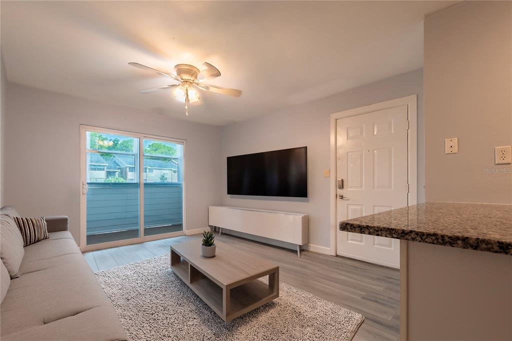 A kitchen features white cabinets, stainless steel appliances, a granite countertop, and gray wood flooring — 1400 GANDY BOULEVARD N UNIT 1010, ST PETERSBURG, FL