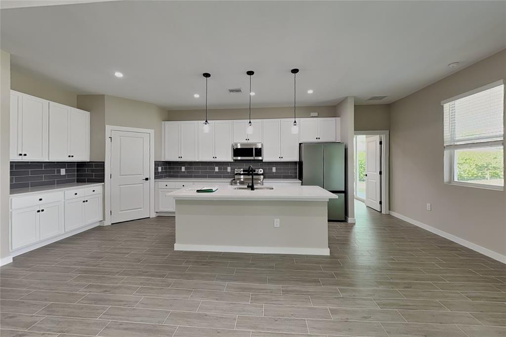 A kitchen features white cabinetry, a central island, stainless steel appliances, and gray tile flooring — 2440 BRONCO LANE, NORTH PORT, FL
