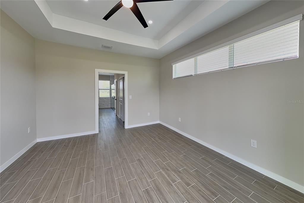 An empty room features light gray walls, wood-look tile flooring, and a tray ceiling — 2440 BRONCO LANE, NORTH PORT, FL