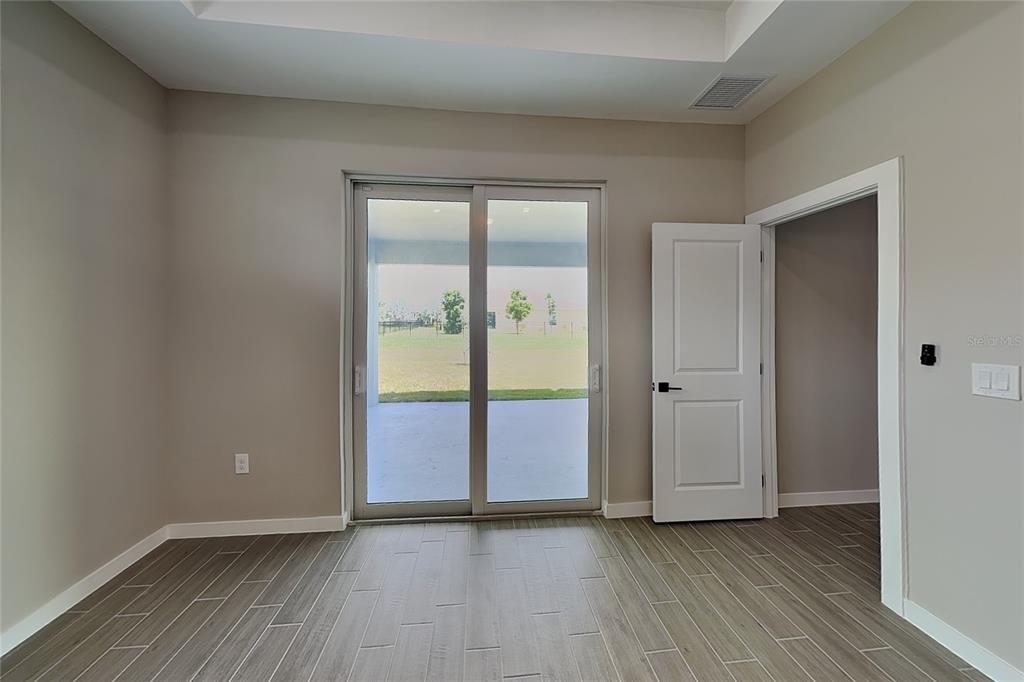 A room with gray wood-look tile flooring, a sliding glass door, and an open doorway — 2440 BRONCO LANE, NORTH PORT, FL