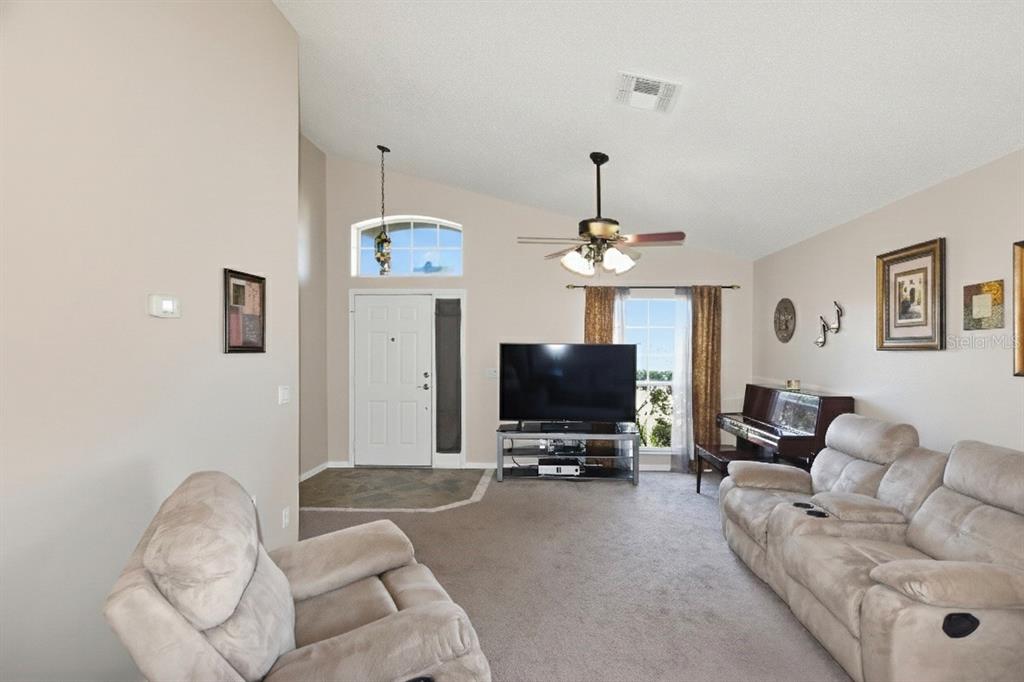 A living room with beige carpet, a vaulted ceiling, a ceiling fan, and a piano — 457 MICKLETON LOOP, OCOEE, FL