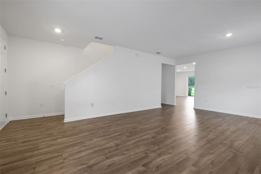An empty room with white walls, wood-look flooring, and a staircase leading to the upper level — 3880 HOLSTEIN WAY, GREEN COVE SPRINGS, FL