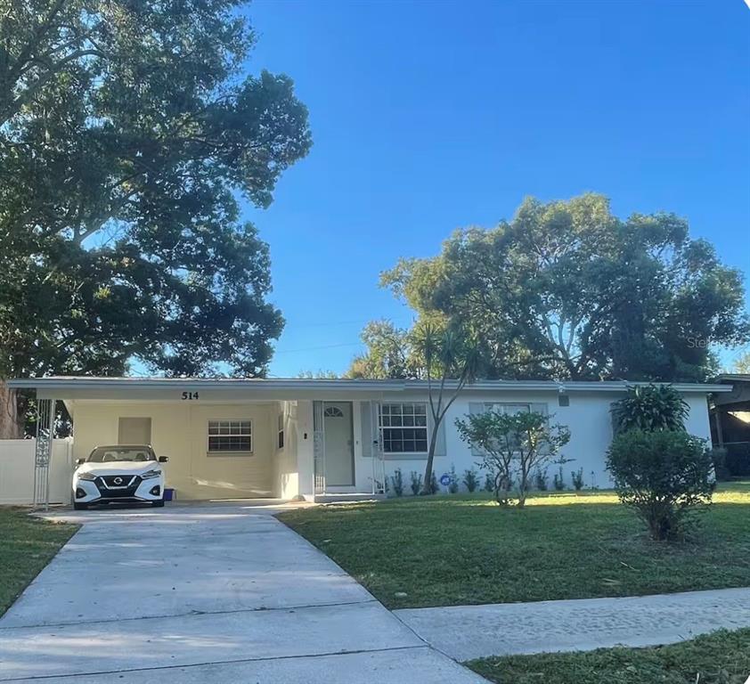 A single-story white house with a carport and a concrete driveway under a clear sky — 514 WIGMAN DRIVE, MAITLAND, FL