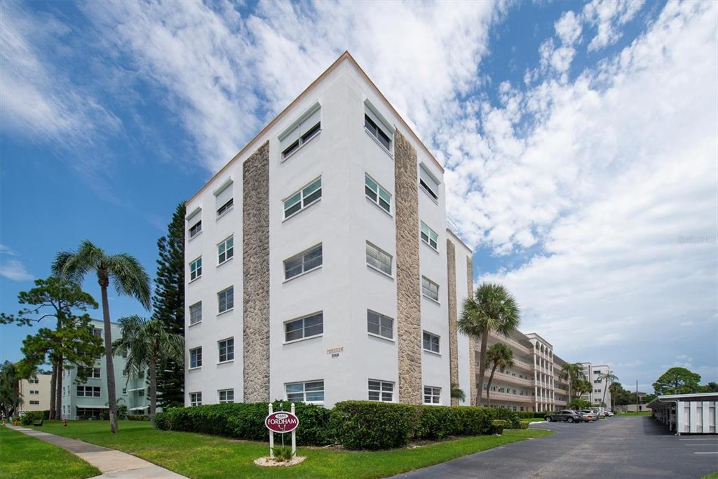 A multi-story white apartment building with stone accents stands next to a parking lot — 5603 80TH STREET N UNIT 415, ST PETERSBURG, FL