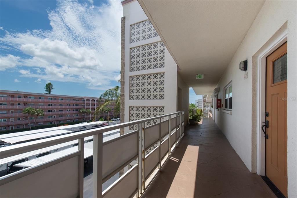 An exterior apartment building walkway features a metal railing, a brown door, and decorative concrete blocks — 5603 80TH STREET N UNIT 415, ST PETERSBURG, FL