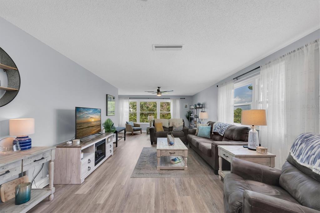 A living room features light wood-look flooring, a gray sofa, and a television on a console — 5603 80TH STREET N UNIT 415, ST PETERSBURG, FL