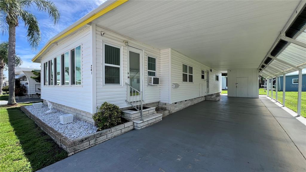 A white mobile home with a large carport and a small landscaped rock garden — 1100 BELCHER ROAD S UNIT 241, LARGO, FL