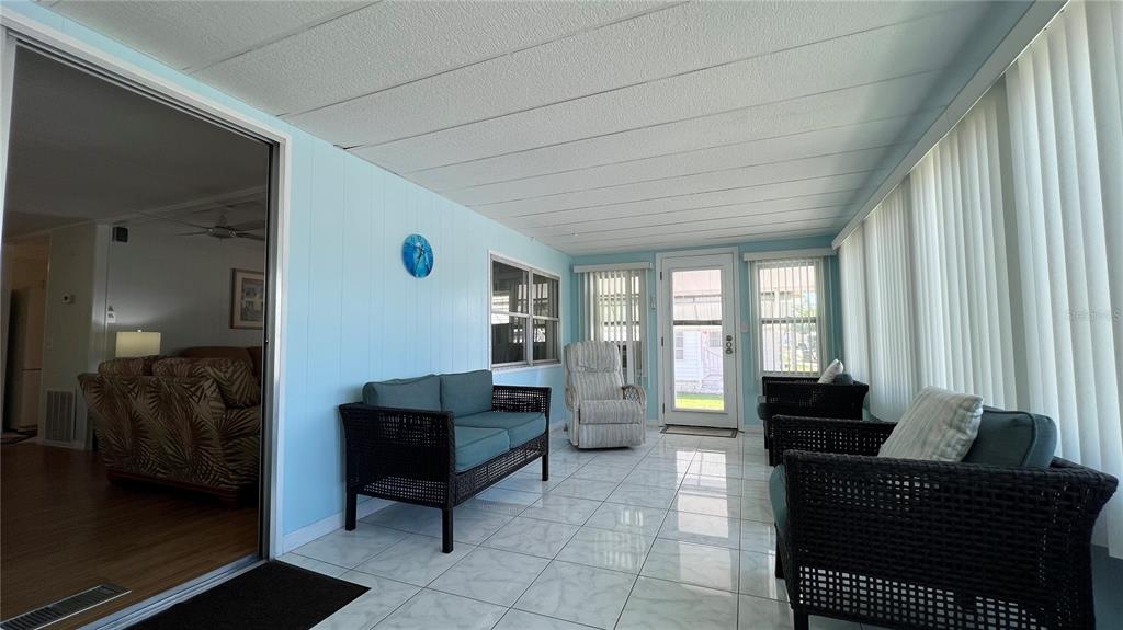 A sunroom with light blue walls, tile flooring, wicker furniture, and vertical blinds — 1100 BELCHER ROAD S UNIT 241, LARGO, FL