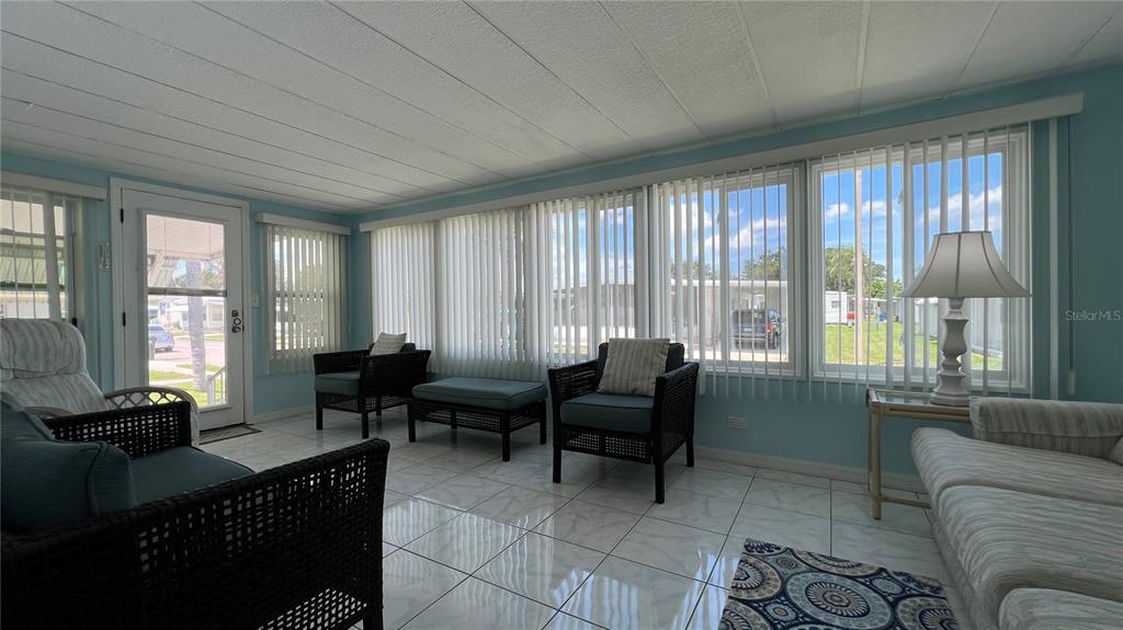 A sunroom features tile flooring, wicker furniture, and large windows with vertical blinds — 1100 BELCHER ROAD S UNIT 241, LARGO, FL