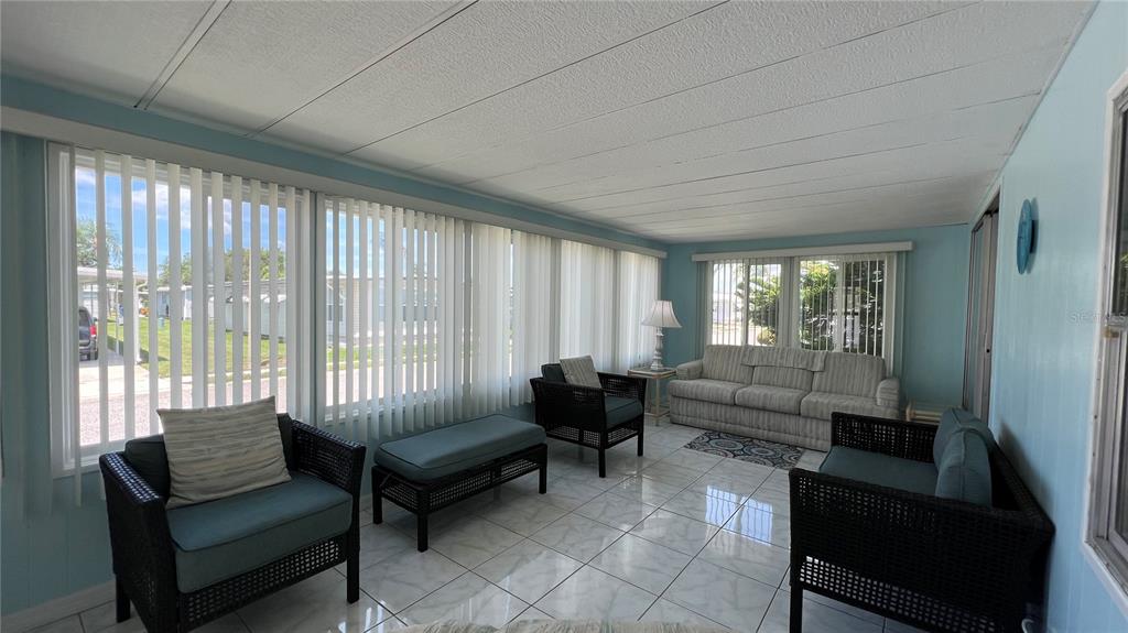 A sunroom features light blue walls, white tile flooring, vertical blinds, and wicker furniture — 1100 BELCHER ROAD S UNIT 241, LARGO, FL