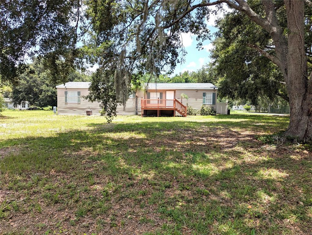 A single-story manufactured home with a wooden deck stands in a grassy, tree-shaded yard — 30517 CLEARVIEW DRIVE, WESLEY CHAPEL, FL